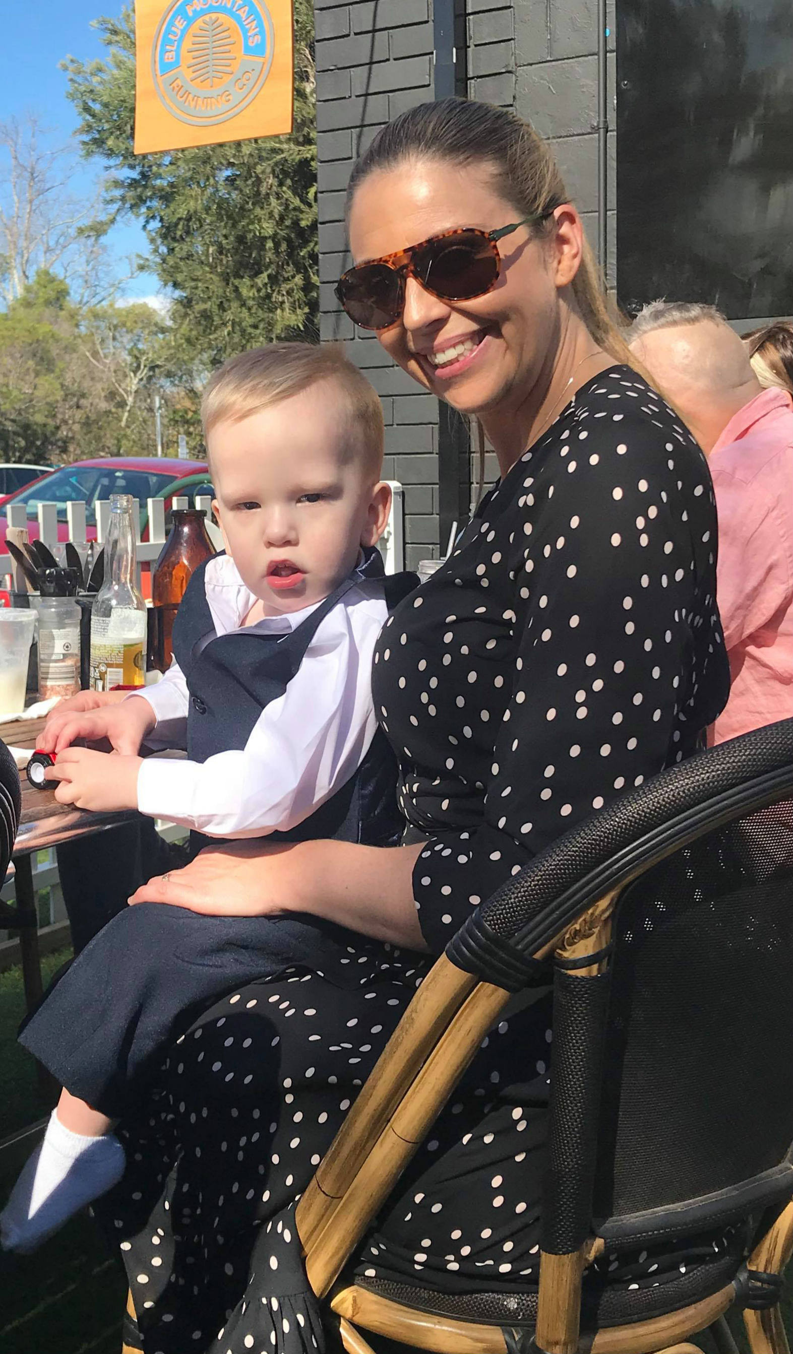 boy toddler sits on his mum's lap at an outdoor cafe